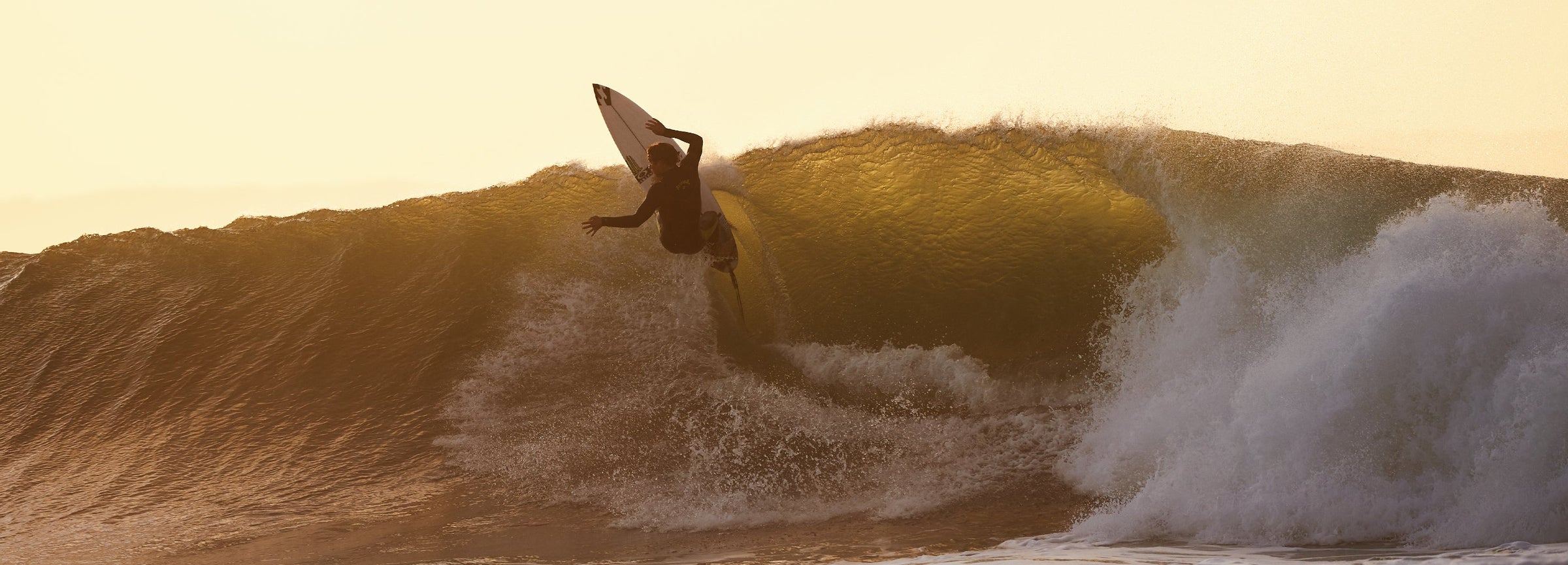 Surfer jumping out of a wave at sunset