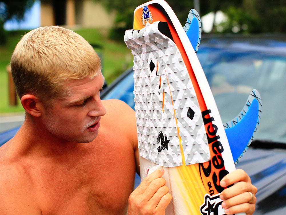 Blond man examines traction pad on surfboard