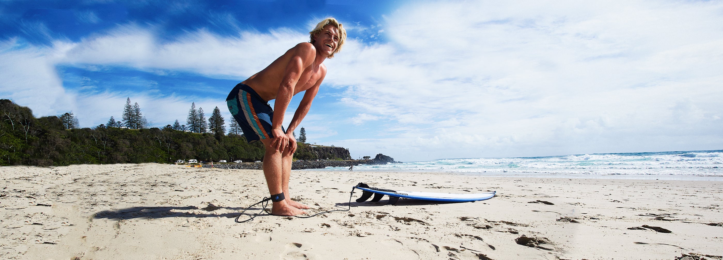 Man standing on beach looking at waves with surfboard at his feet