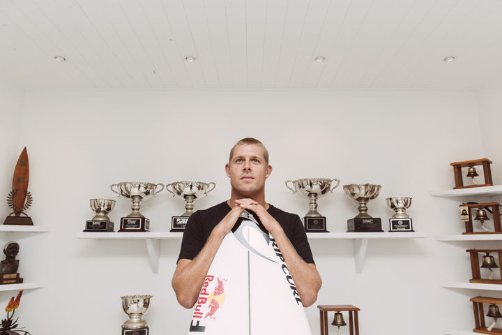 Man holding surfboard while surrounded by trophys
