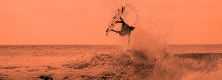 Orange toned pic of man jumping out of wave on surfboard