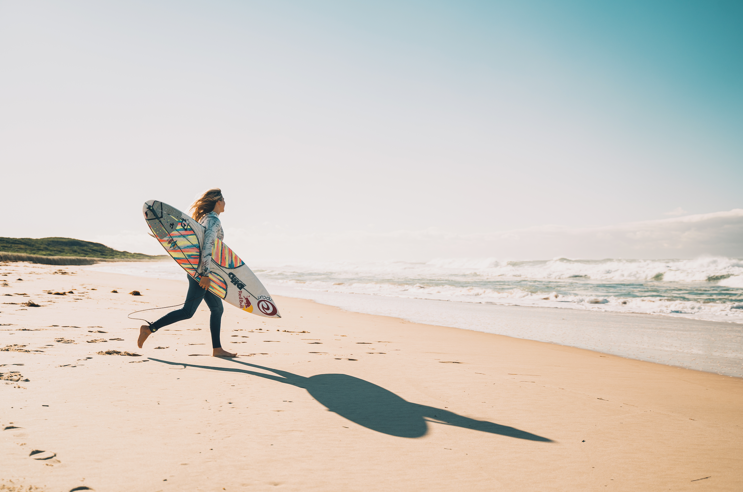 Girl running into waves with surfboard