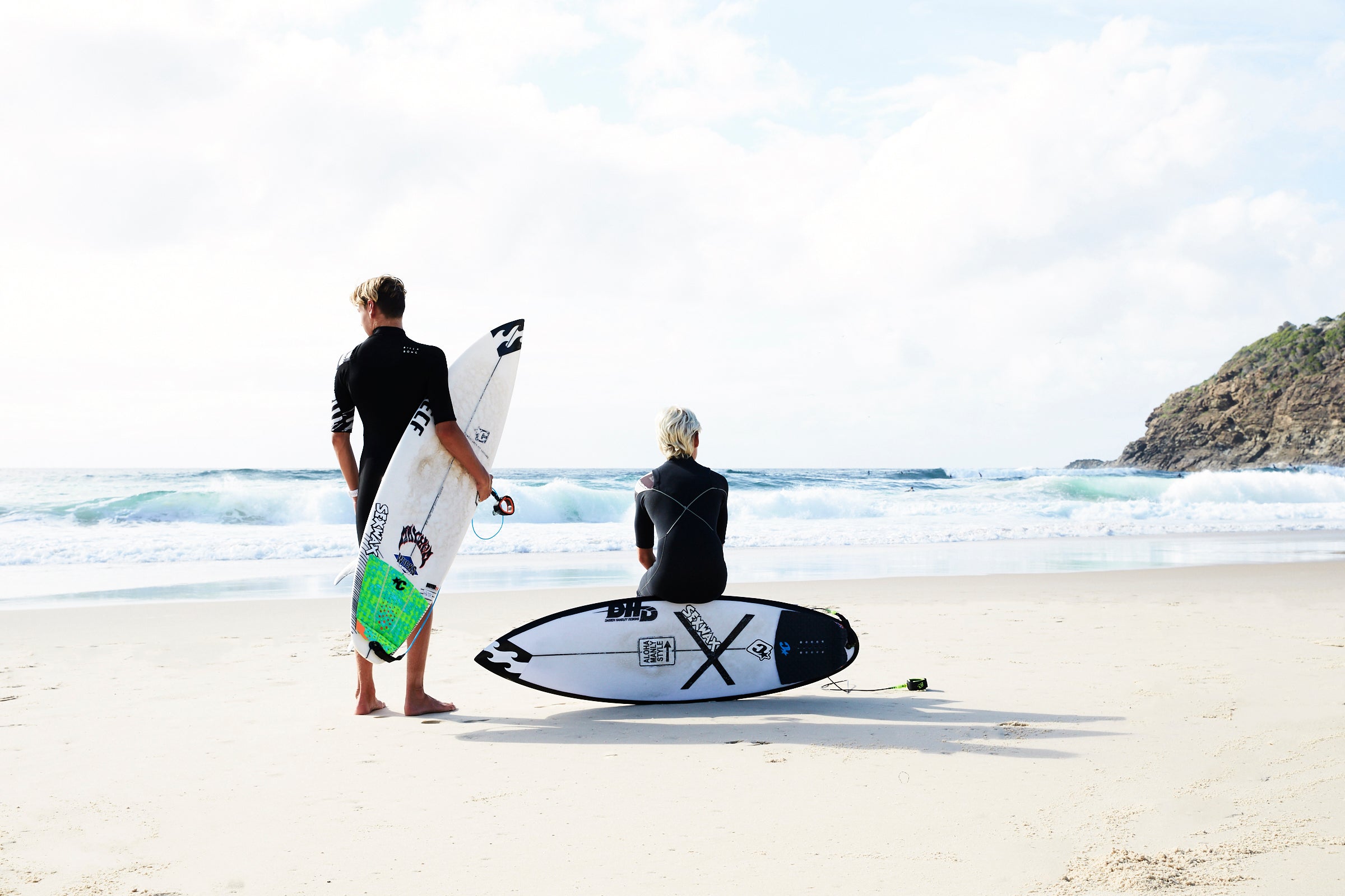 two boys sitting on the beach with surfboards